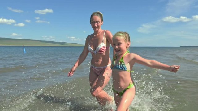 Mom and her children are running into the water. They run along the water.