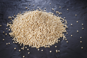 Quinoa grains with spoon and bowl on black background