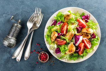 Fresh vegetable salad bowl of tomatoes, cucumbers, italian mix, lettuce and grilled chicken breast on table. Fried chicken meat, fillet with salad. Healthy food