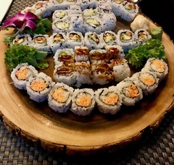 Delicious Sushi Plate with an assortment of different roles including salmon, shrimp, cucumber and avocado maki and sashimi decorated with a beautiful orchid flower