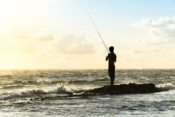 Sunrise Rock Fishing at the Beach in Oahu, Hawaii - a Man's Silhouette Casting Out a Line Against the Crashing Waves of the Ocean