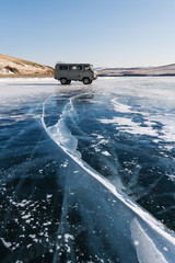 Travelling in winter at frozen lake Baikal in Siberia, Russia. Tourist van parking on ice with cracked line