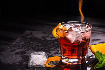 Mezcal Negroni cocktail with flames. Smoky Italian aperitivo. Orange peel.