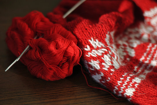 Needlework. Homemade knitting from red and white wool with knitting needles. Close-up.