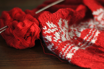 Needlework. Homemade knitting from red and white wool with knitting needles. Close-up.