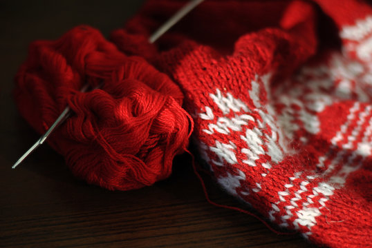 Needlework. Homemade knitting from red and white wool with knitting needles. Close-up.