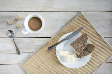 Butter and bread for breakfast, with cup of coffee on rustic wooden background.