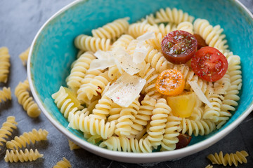 Close-up of boiled fusilli pasta with fresh cherry tomatoes and parmesan served in a blue bowl, selective focus