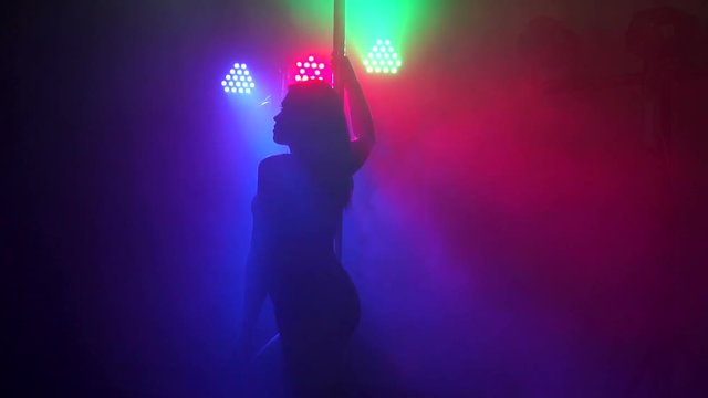 Sexy girl spinning around a pole in a dark room in slow motion. Pole dance.
