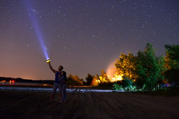 A guy with a girl shines a flashlight at the sky