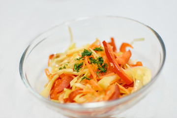 healthy food for diets: vegetarian vegetable salad from fresh cabbage, carrots, bell pepper and dill. Salad in transparent bowl on white background