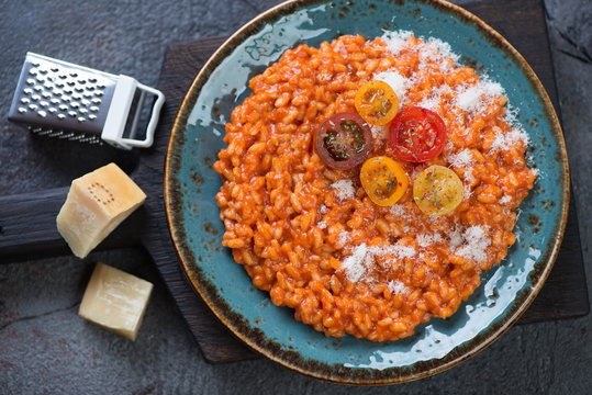 Top view of tomato risotto served in a turquoise plate with addition of fresh cherry tomatoes and grated parmesan cheese