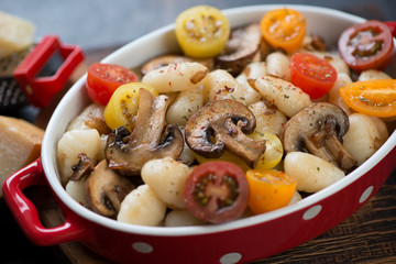 Close-up of boiled potato gnocchi with roasted mushrooms and fresh sliced cherry tomatoes served in a bowl, selective focus