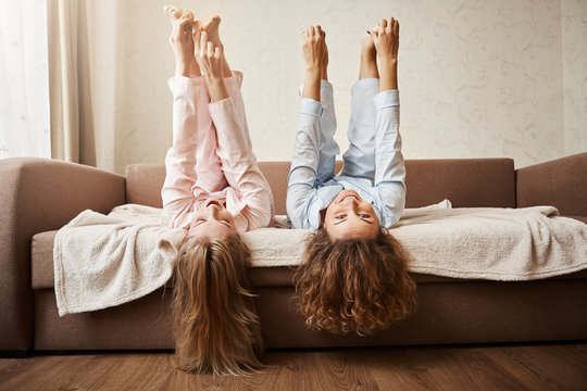 Dare You To Touch Feet While Lying. Portrait Of Adorable Women Fooling Around And Being Childish At Home In Nightwear, Lie On Sofa, Lifting Feet And Touching It With Hands In Playful Mood