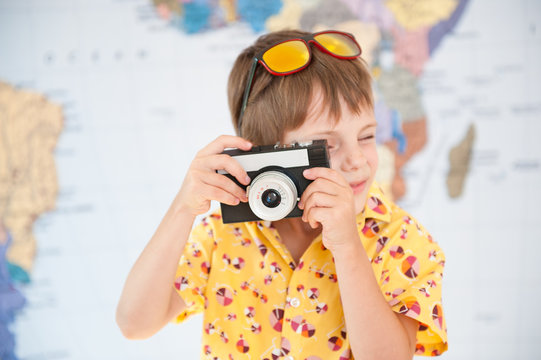 handsome little kid in yellow shirt and sunglasses takes shot with vintage camera on world map background