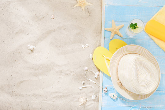 Top view straw hat, flip flops, sheadphones, sunblock, towel, seashells, summer cocktail with copy space. Traveler accessories on sand. Travel vacation concept. Summer background