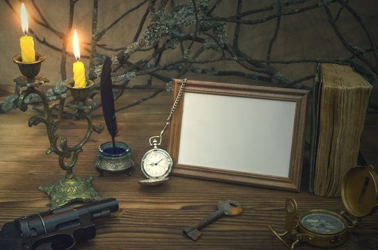 Empty photo frame with copy space and diary book of adventurer on wooden table with compass and rusty key in the light of burning candle.. Traveller concept. Explorer.