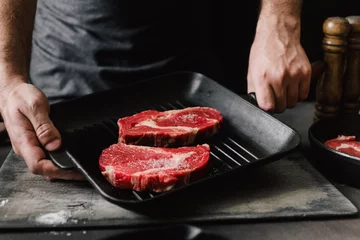 Crédence de cuisine en verre imprimé Cuisinier Man cooking beef steaks Male hands holding a grill pan with beef steaks on kitchen