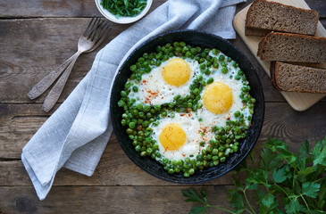 Fried eggs with green peas in a frying pan