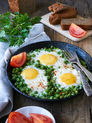 Fried eggs with green peas in a frying pan