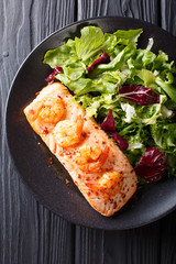 Delicious food: baked salmon with prawns in honey sauce and fresh salad on a plate close-up. Vertical top view