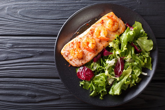 Baked salmon with prawns and honey sauce with a side dish of salad mix close-up on a plate. horizontal top view