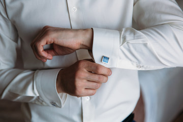 Groom hands hold cufflinks. Elegant gentleman clother, white shirt and black belt