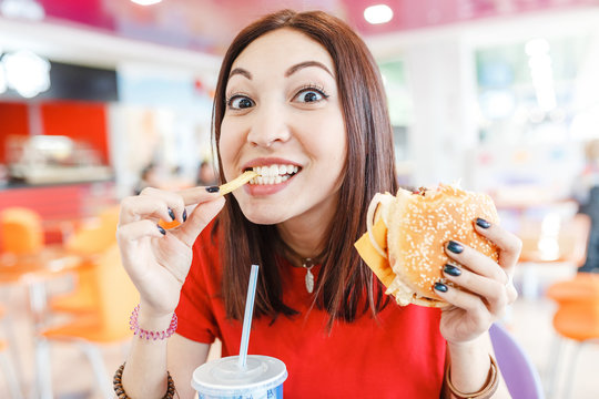 Happy Young Woman Having Hamburger, Soda Drink And French Fries In Fast Food Restaurant