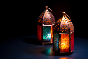 Two colorful oriental Lamp lanterns burn with candles with color reflection on dark black...