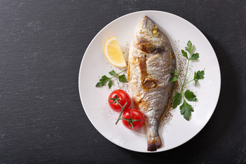 plate of baked fish with vegetables on dark background