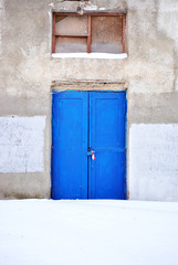 Closed blue painted door with window, gray plaster on wall, grunge background, winter snowy street, vertical