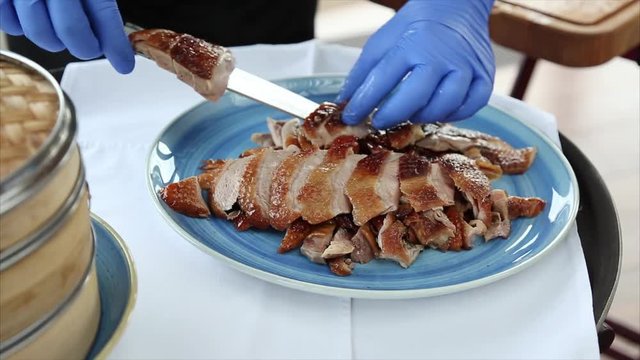 The chef puts the meat of a Peking duck on a plate in a restaurant