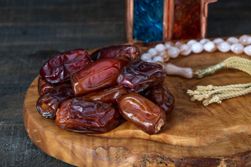 Close up of large premium dates on wooden board and rosary with oriental Lantern lamp on wood background. Islamic Holy Month Greeting Card, Ramadan Kareem
