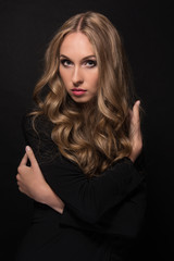 Fototapeta premium Portrait of a beautiful young sexy girl with long blond hair and evening make-up on a black background.