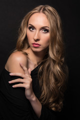 Portrait of a beautiful young sexy girl with long blond hair and evening make-up on a black background.