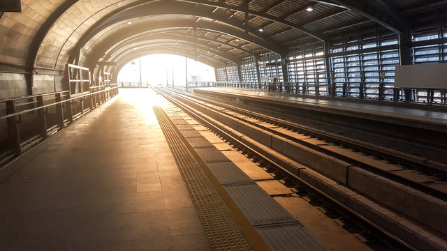 Empty modern train station platform with sunlight streaming through arched roof highlighting urban transportation and travel concept - Powered by Adobe