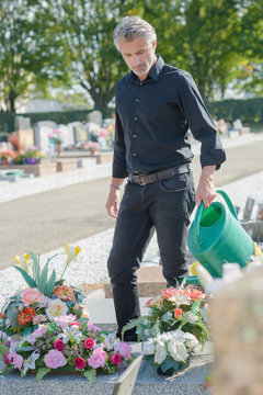 man watering flowers in cemetery