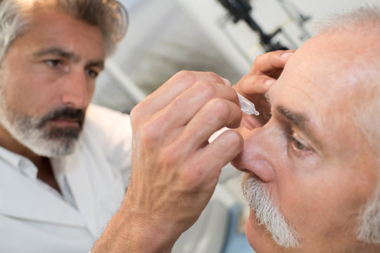 doctor dripping eye drops to senior patient