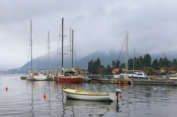 Naklejka premium Misty Mediterranean landscape. Yachts and fishing boats on the water near seaside village of Seljanovo. Montenegro, Bay of Kotor (Adriatic Sea), Tivat