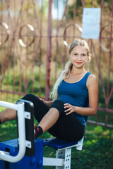 Fit woman in a blue shirt and leggings exercising at outdoors gym playground equipment. fit and sporty woman training outside