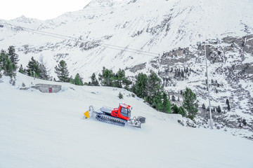 Red bully pisten on snow track for skiers with pine tree and mountain background