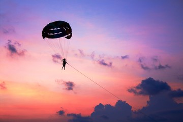 Silhouette of two people on parachute against the sunset sky of all colors of the spectrum