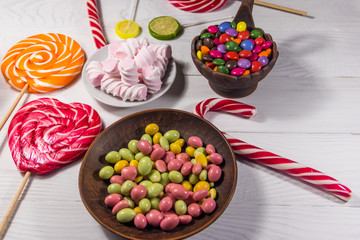 Colorful chocolate candies, lollipops, candy cane and marshmallows on wooden table