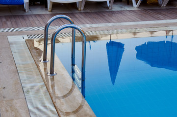 Pool with perfectly blue water at the resort. Alluring cool water on a hot summer day. A typical vacation is all inclusive in Turkey, Egypt, Tunisia. The water reflects the cafe, umbrellas.