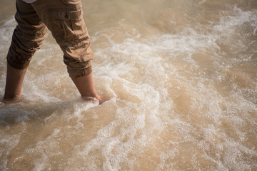 close-up leg of man is standing on the beach with wave from sea in morning at summer.