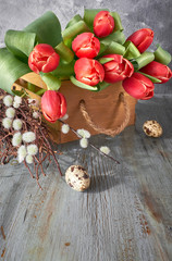 Spring celebration background: bunch of red tulips, spring decorations and painted eggs on gray rustic wood