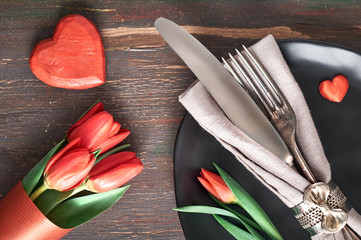 Springtime menu concept with light yellow plate and cutlery decorated with fresh tulips on dark wood