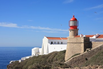 Fototapeta na wymiar Lighthouse on Sagres cape on bright blue sky background. Seagulls in the sky.