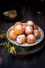 On a plate donuts with sugar powder, decorated with mimosa flowers. Wooden background