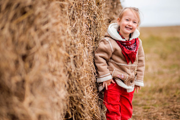Naklejka na ściany i meble a little cheerful girl next to a haystack